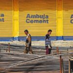 Laborers carry iron rods as Ambuja Cement advertisement is seen on the closed shutters near a construction selling items area in Sopore, District Baramulla, Jammu and Kashmir, India on 14 April 2022. (Photo by Nasir Kachroo/NurPhoto via Getty Images)