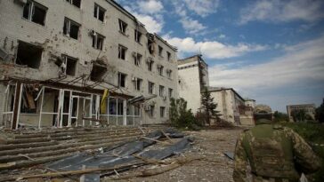 A Ukrainian serviceman walks next to a building damaged by a Russian military strike, as Russia