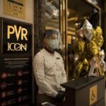 An employee wears a protective mask while waiting to greet customers outside the PVR Icon cinema at the DLF Promenade Mall in New Delhi