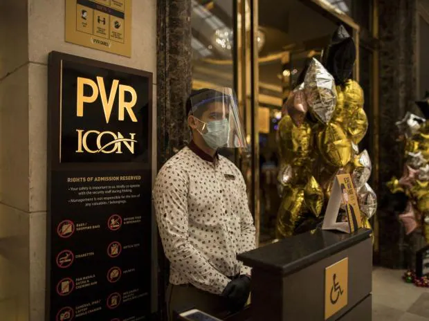 An employee wears a protective mask while waiting to greet customers outside the PVR Icon cinema at the DLF Promenade Mall in New Delhi