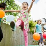 Mother and daughters playing in garden with balloons obstacle course -