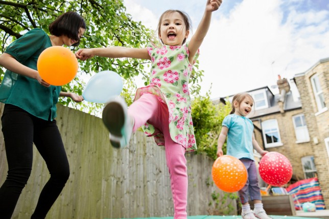 Mother and daughters playing in garden with balloons obstacle course -