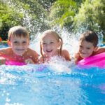 Portrait of three children splashing on inflatable mattress in garden swimming pool