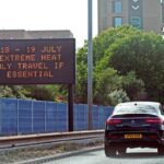 A car driving on the motorway next to a sign warning about extreme heat.