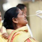 A healthcare worker collects a nasal swab sample of a woman for a COVID-19 test amid a surge in coronavirus cases, in Jammu.