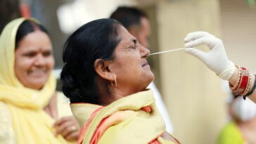 A healthcare worker collects a nasal swab sample of a woman for a COVID-19 test amid a surge in coronavirus cases, in Jammu.