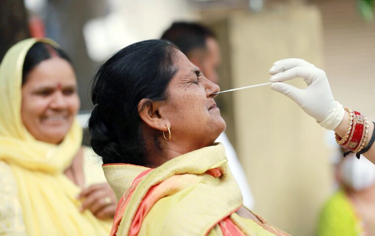 A healthcare worker collects a nasal swab sample of a woman for a COVID-19 test amid a surge in coronavirus cases, in Jammu.