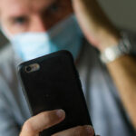 man with face mask in home quarantine lockdown checking pandemic news