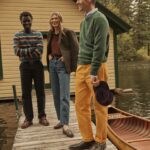 Two men and a woman, three models dressed in prep, stand next to a canoe.