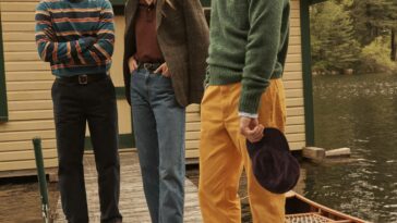 Two men and a woman, three models dressed in prep, stand next to a canoe.