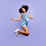 Bottom view portrait of crazy positive girl in jeans outfit jumping in air enjoying daydream having weekend vacation holiday isolated on violent background. Luck success concept