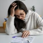 Woman looking worried while checking electricity bill at home.