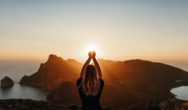 Young woman in spiritual pose holding the light in front of mountains