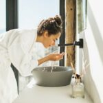 Young woman awakening, washing and cleaning her face with splashing water