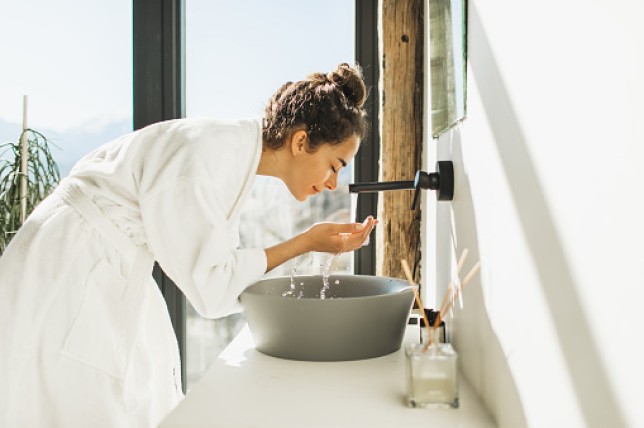 Young woman awakening, washing and cleaning her face with splashing water