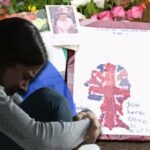 person sad on backdrop of flowers and signs for queen