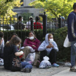 Migrants from Central and South America wait near the residence of Vice President Kamala Harris after being dropped off.