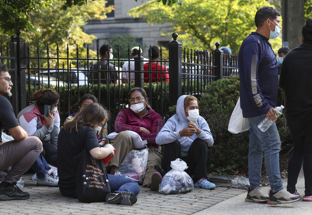 Migrants from Central and South America wait near the residence of Vice President Kamala Harris after being dropped off.