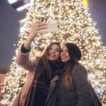 Two friends taking a selfie in front of a Christmas Tree