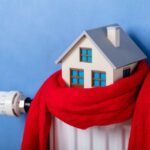 Close-up Of Heating Radiator With Model House And Knitted Scarf In Front Of Blue Wall