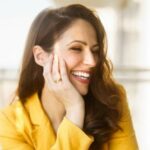 Nic Thorp in yellow suit laughing with her head turned from the camera and resting on her right arm