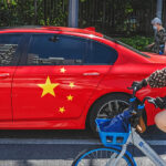 BEIJING, CHINA - JULY 08: A woman rides her bike passed a BMW painted with the national flag of China on it in the street on July 8, 2021 in Beijing, China. (Photo by Kevin Frayer/Getty Images)