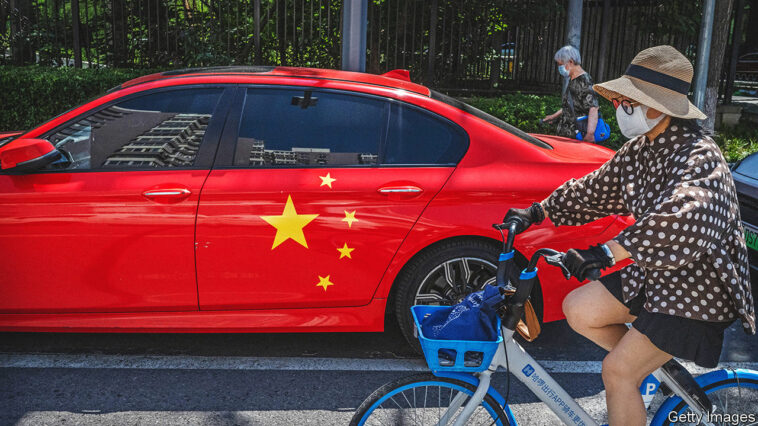 BEIJING, CHINA - JULY 08: A woman rides her bike passed a BMW painted with the national flag of China on it in the street on July 8, 2021 in Beijing, China. (Photo by Kevin Frayer/Getty Images)