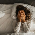 Woman lying in bed with her hands over her face.