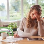 Worried Woman With Digital Tablet Sitting At Table At Home Reviewing Finances