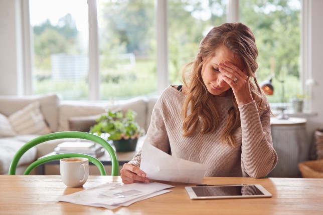 Worried Woman With Digital Tablet Sitting At Table At Home Reviewing Finances