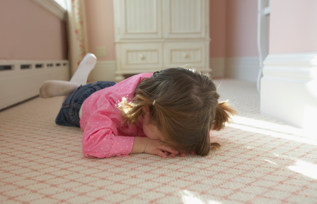 Young girl laying on bedroom carpet covering face