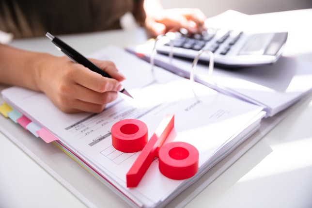 Close-up Of Red Percentage Symbol With Businessperson Calculating Bill