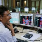 A broker laughs while speaking to a colleague, as they trade on their computer terminals at a stock brokerage firm in Mumbai