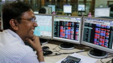 A broker laughs while speaking to a colleague, as they trade on their computer terminals at a stock brokerage firm in Mumbai