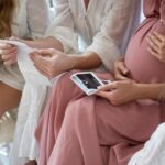 Hands of pregnant woman with friends holding ultrasound scan result at baby shower