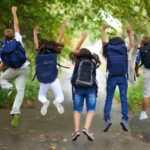 Children wearing backpacks jumping into the air