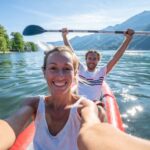 Young couple taking selfie portrait in red canoe on mountain lake