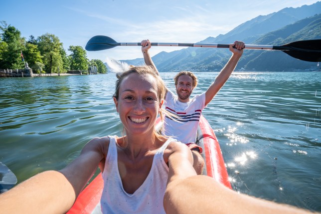 Young couple taking selfie portrait in red canoe on mountain lake