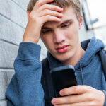 A teenage boy upset looking at his smartphone.