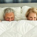 Senior couple relaxing in bed hiding under sheets