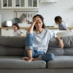 Exhausted mother sitting on couch while kids running at home