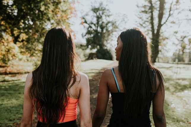 Two young woman walking through a sunny park