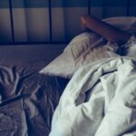 A woman trying to sleep more, having trouble sleeping due to noise, covering her ears with pillow ...