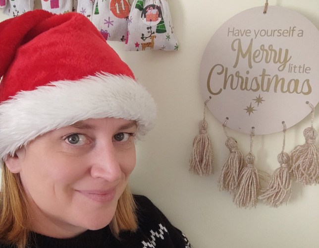 Kirsty in a Christmas hat, standing next to a sign saying 'have yourself a merry little christmas'