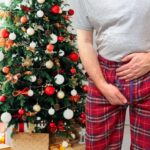 A man holding his pelvic area, while stood in front of a Christmas tree