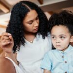 Mother with crying child sitting on floor in living room and talking after tantrum.