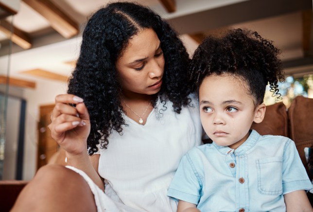 Mother with crying child sitting on floor in living room and talking after tantrum.