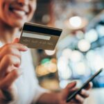 A woman holding a credit card and a phone and smiling