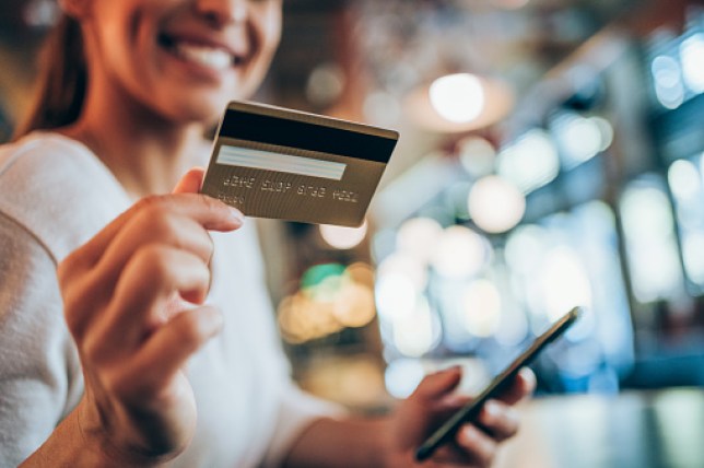 A woman holding a credit card and a phone and smiling