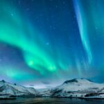 Aurora borealis over in the dark night sky over the snowy mountains in the Lofoten